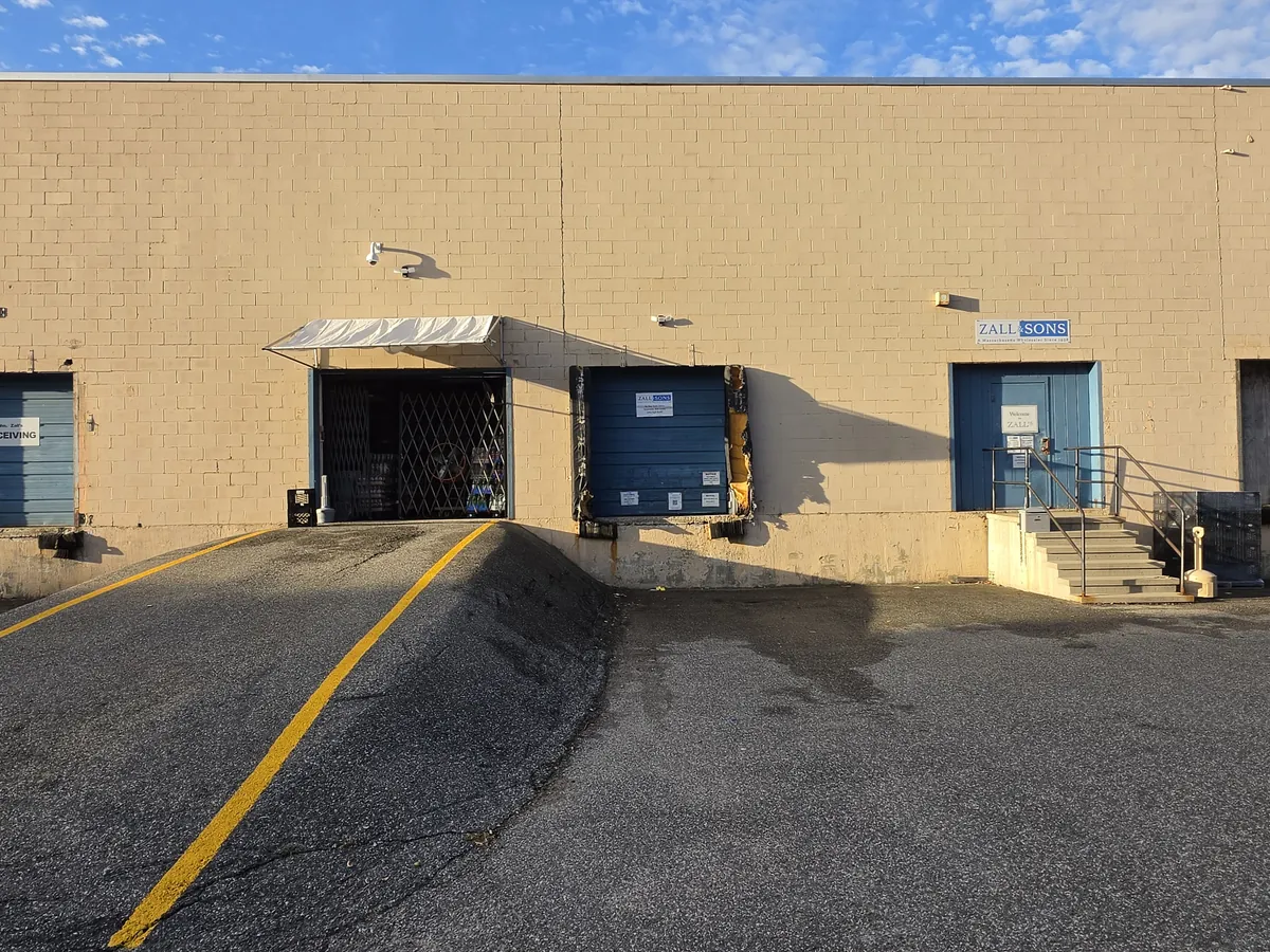 The back of 65 Bay State Drive: loading bays on the left, and the Zall & Sons sign over a blue door with steps on the right